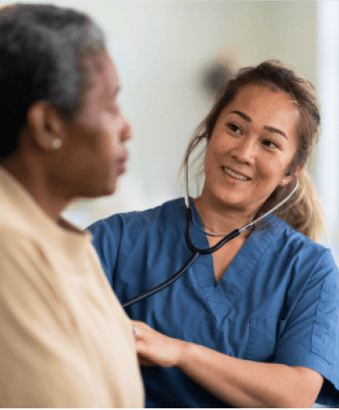 Healthcare professional in blue scrubs using a stethoscope while providing care to a patient